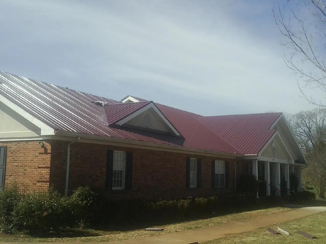 Red metal roof with gabled entries on a long brick building, from a Hail Damage Roof Repair job in Groton