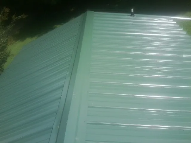 New green metal panels meeting at the ridge of a roof — Flat Roof Repair work by our crew in Groton