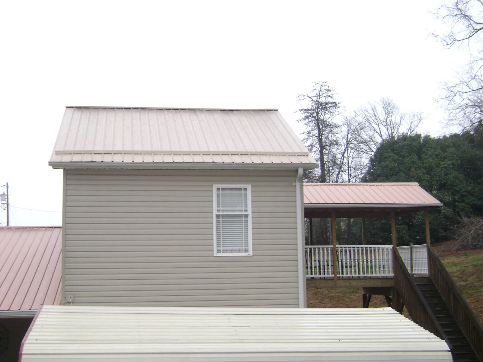 Tan metal roofs on a two story addition and attached porch, from a Roof Replacement job in Groton